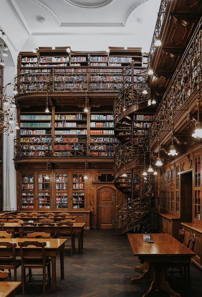 Historic library interior with ornate wooden bookshelves, spiral staircase, and wooden tables in a stunning bookstore setting.