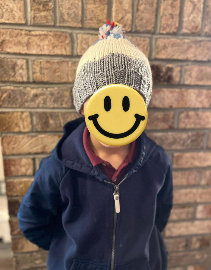 Child wearing a knitted hat and navy jacket with a smiley face covering, symbolizing teachers showing love for students.