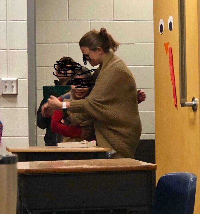 Teacher showing love for students, warmly embracing children in a classroom decorated for a festive occasion.