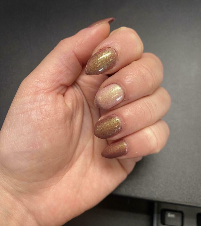 Close-up of a human hand with shiny brown iridescent nail polish showcasing unique details of the human body.
