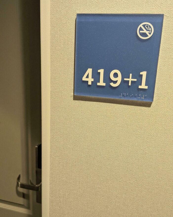 Hotel room sign with creative number design 419+1 and no smoking symbol on textured wall in modern hotel interior.