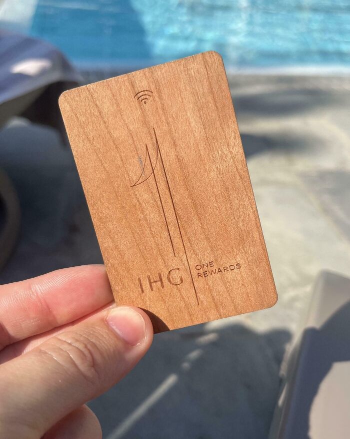 Hand holding a wooden key card by a pool, showcasing a creative hotel design decision with natural material use.