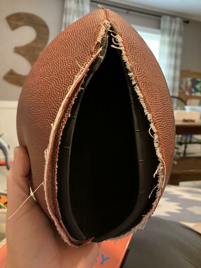A close-up of a hand holding a football that has split open, showing a hilariously unlucky parenting moment.