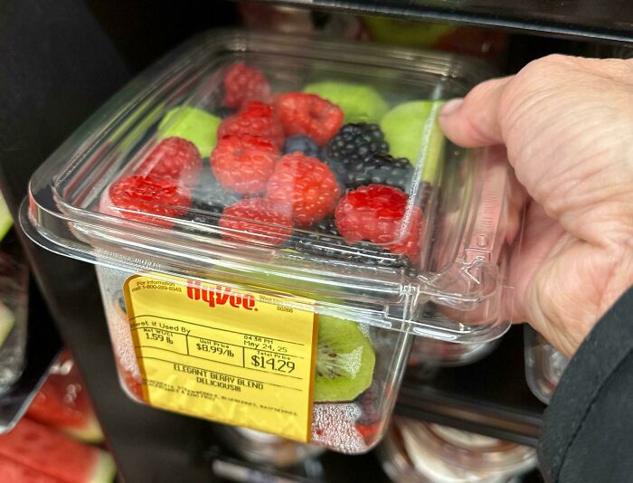 A hand holding an expensive mixed berry fruit container showing tariff costs affecting Americans’ wallets.