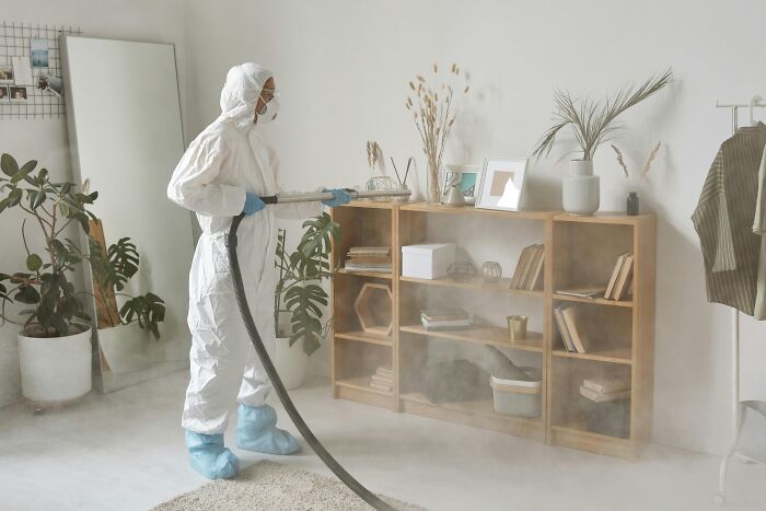 Person in protective suit sanitizing a home interior, illustrating hidden costs of buying a home many don’t consider.