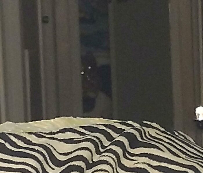 Dimly lit room with a faint ghostly figure and glowing eyes peeking from the dark doorway, evoking chilling ghost encounters.