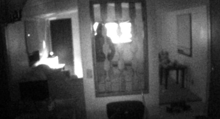 Dimly lit room with a shadowy figure in a window, evoking chilling ghost encounters and eerie paranormal activity at night.