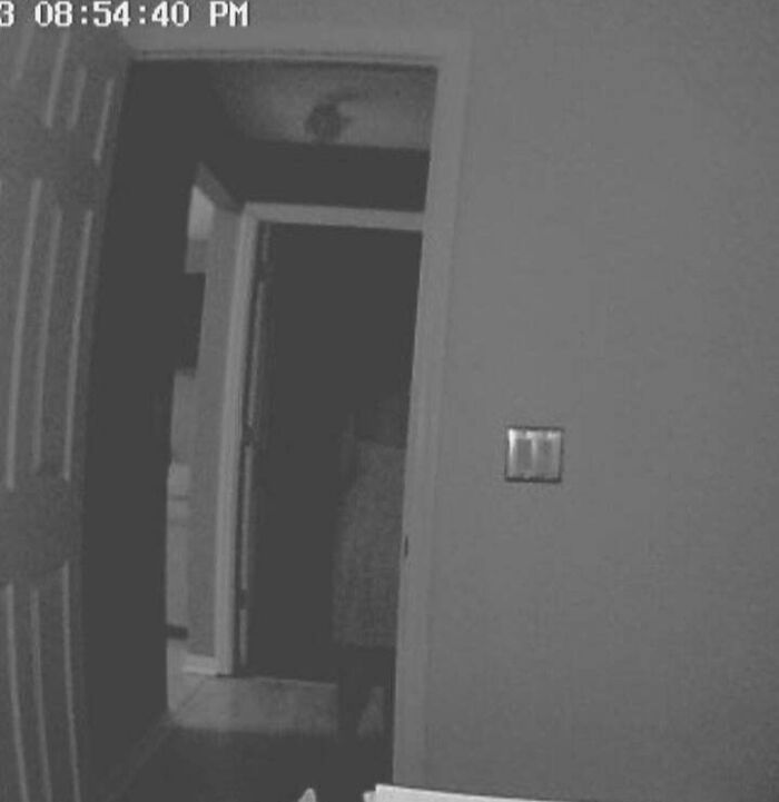 Black and white security camera image showing a shadowy figure in a dark doorway, illustrating chilling ghost encounters.