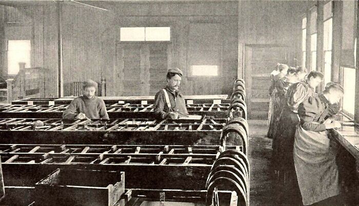 Vintage photo of American working class people focused on their jobs inside a factory with wooden machinery.