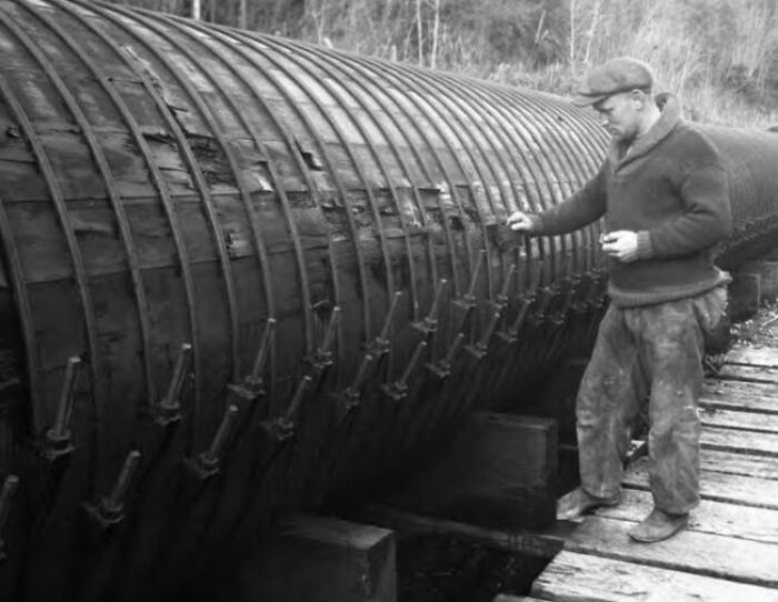 Vintage photo of an American working class man inspecting large industrial equipment outdoors on a wooden platform.
