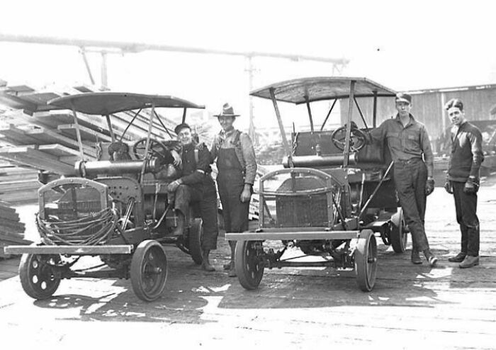 Four American working class men posing with vintage motor vehicles at a job site in a black and white photo.