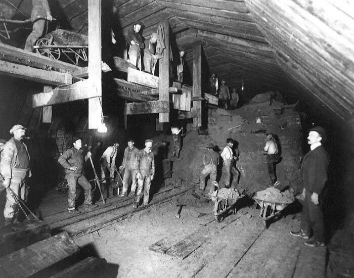 Vintage photo of American working class people laboring in an underground mine, using wheelbarrows and hand tools.