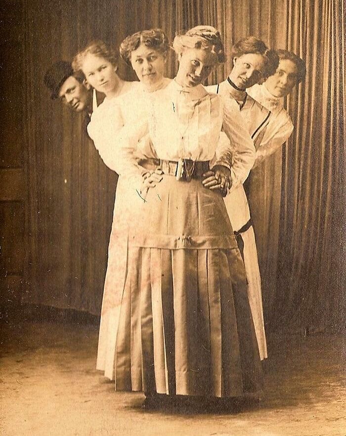 Victorian times group portrait showing five women and a man in period clothing posing behind each other indoors.