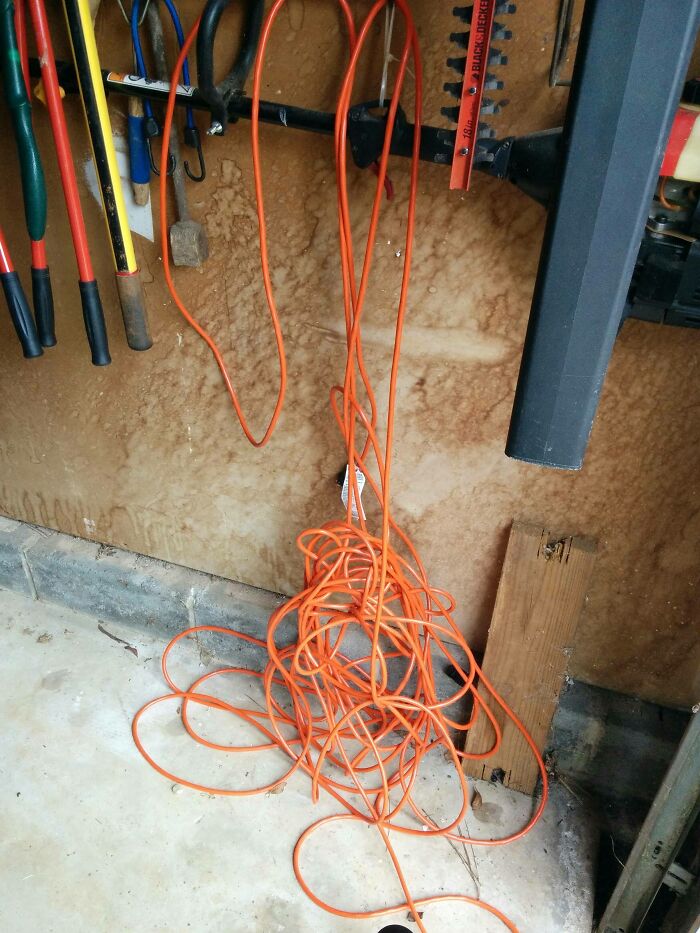Tangled orange extension cord in a cluttered garage corner with various tools hanging above, showing careless damage.