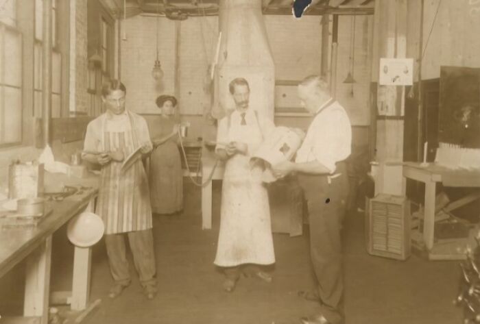 Vintage photo of American working class people in a workshop, wearing aprons and engaged in their jobs.