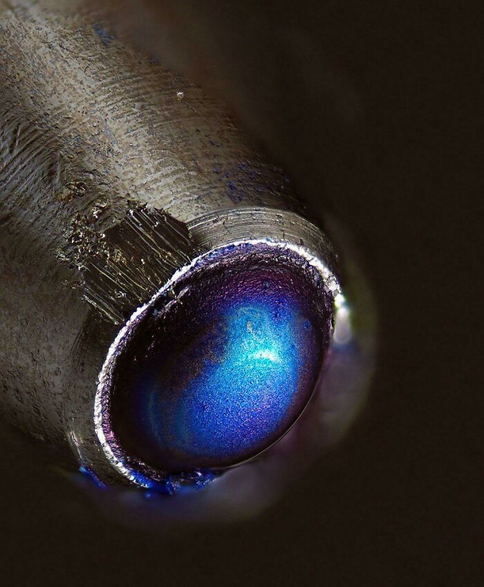 Close-up microscopic image of a pen tip showing detailed texture and a vibrant blue ink ball for a different perspective.