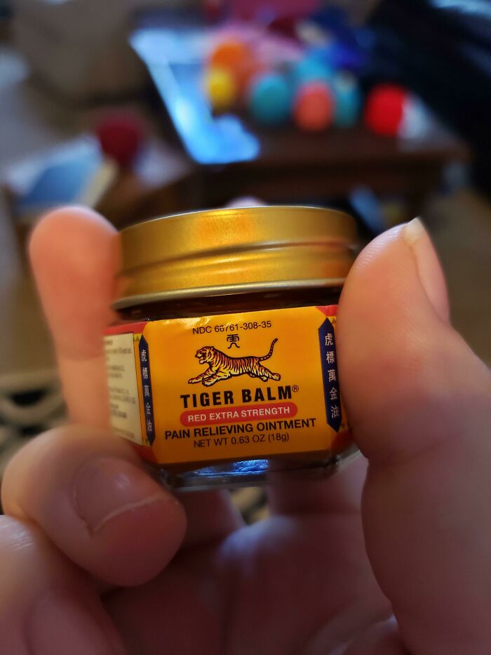 Hand holding a small jar of Tiger Balm pain relieving ointment, shown as a useful travel hack item.
