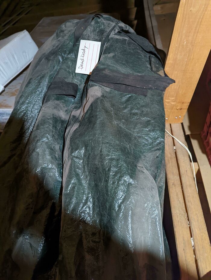 Dusty black bag with a "Dead body" tag found hidden in an old house among cool buried and forgotten items.