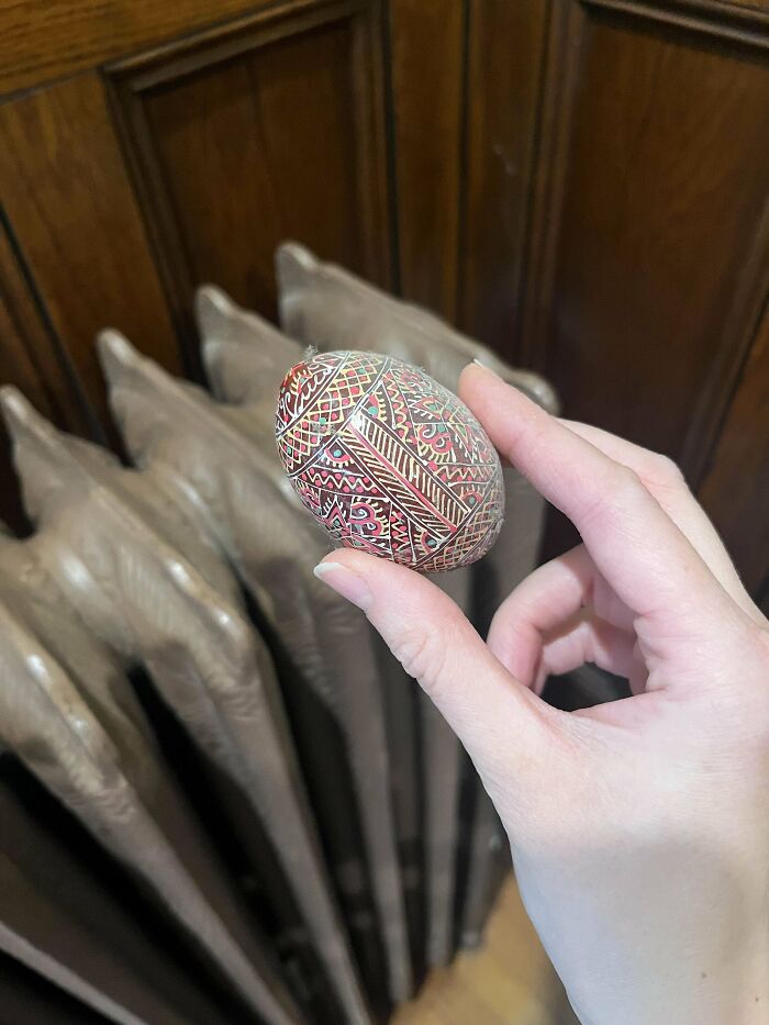 Hand holding a small, intricately decorated egg found hidden in an old house with a vintage radiator in the background.