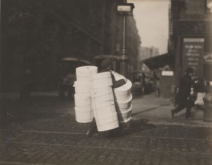 Vintage photo of an American working class person carrying multiple hat boxes on a city street during work.