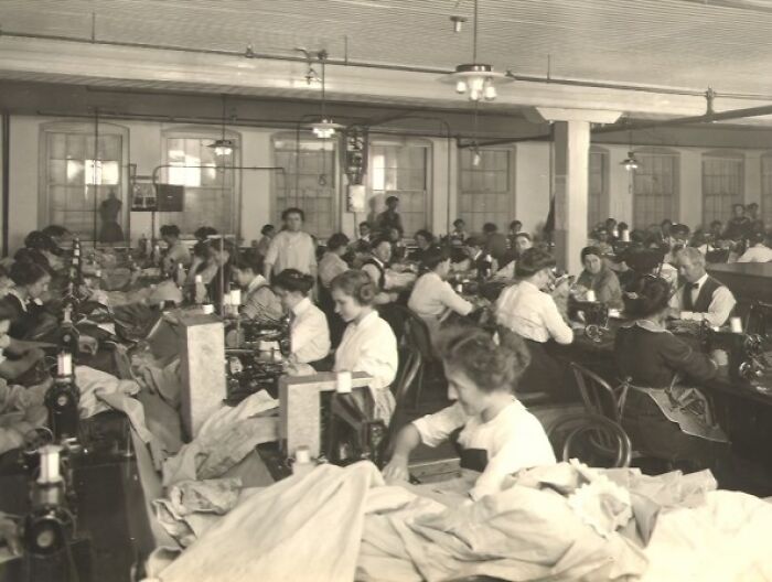Vintage photo of American working class people sewing and managing textiles in a crowded factory during their jobs.