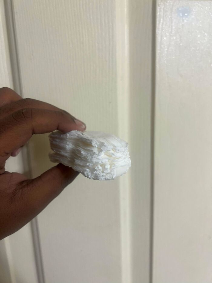 Hand holding a layered white object against a beige background in a funny pic showing utter confusion.