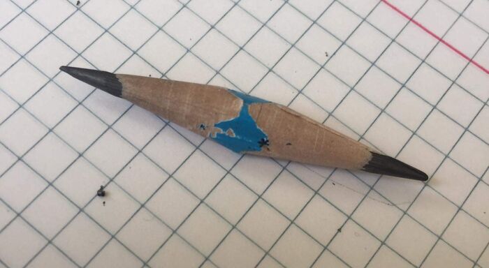 Broken pencil damaged by people borrowing it, showing signs of heavy use and wear on a grid-patterned surface.