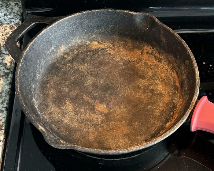 Rusty and damaged cast iron skillet left on stovetop, showing signs of neglect and wear from borrowing.