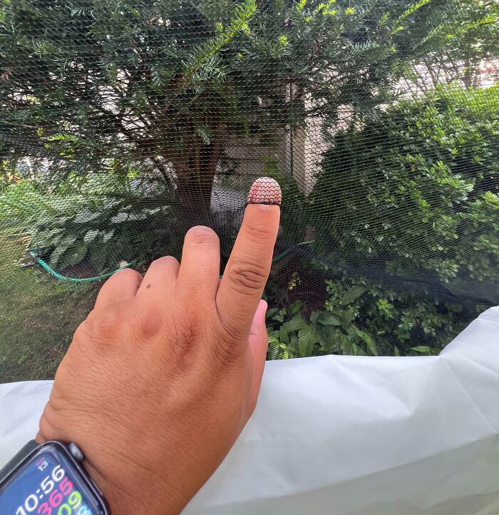 Hand with smartwatch showing fingertip caught in a damaged torn mesh screen, illustrating people damaging things they borrowed.