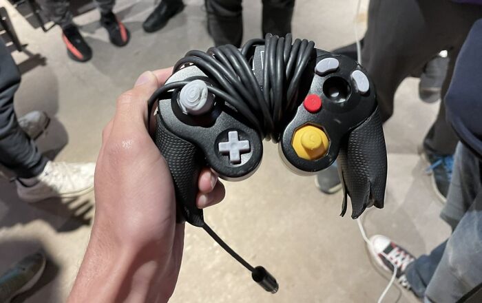 Hand holding a damaged game controller with a broken grip and tangled cable, showing infuriating pics of people damaging things borrowed.