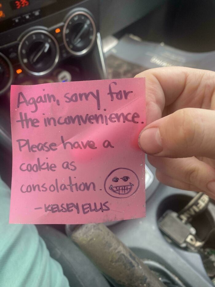 Hand holding a pink note offering a cookie as consolation for an inconvenience, a funny pic causing confusion.
