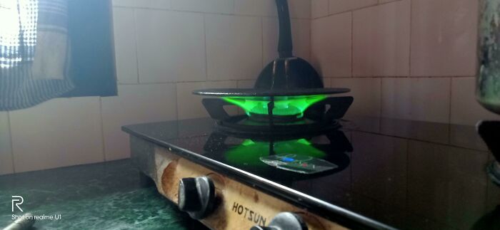 Green gas stove burner lit with a pan on top, a funny pic capturing an utterly confused moment in cooking.