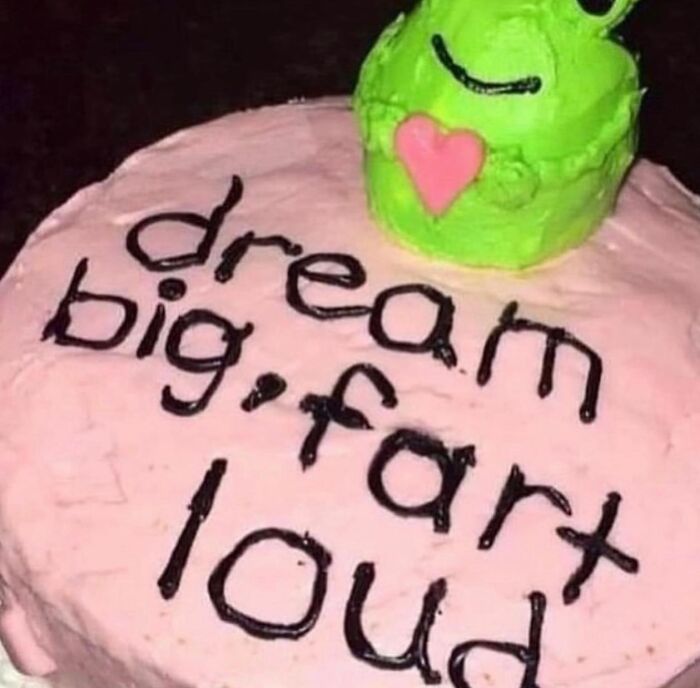 Pink cake with the phrase dream big fart loud and a green frog decoration, an example of disgusting food pics that might ruin appetite