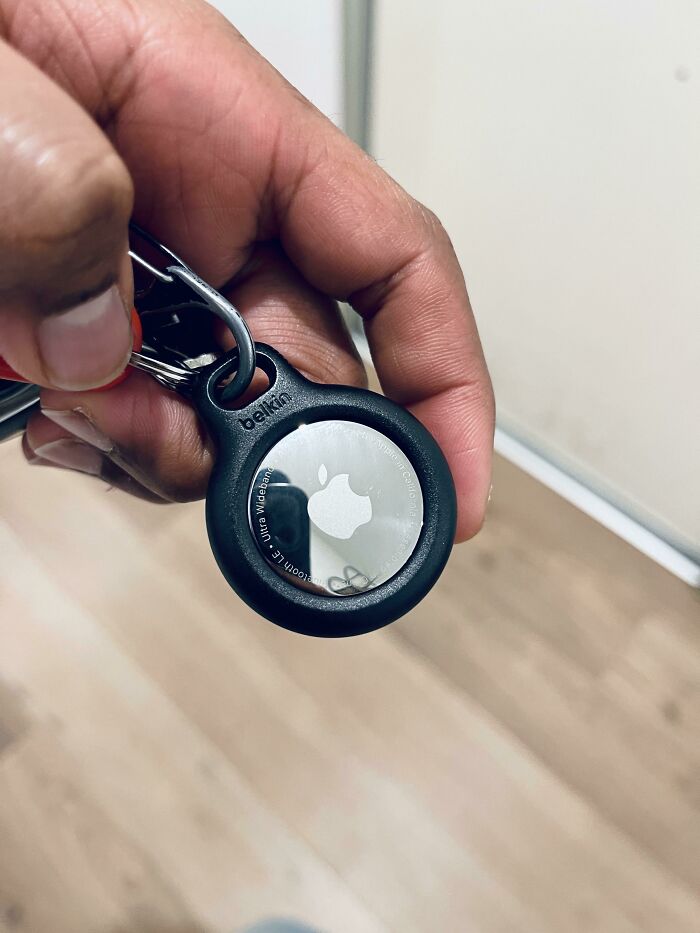 Hand holding a keychain with an Apple AirTag inside a black protective travel case for easy tracking.