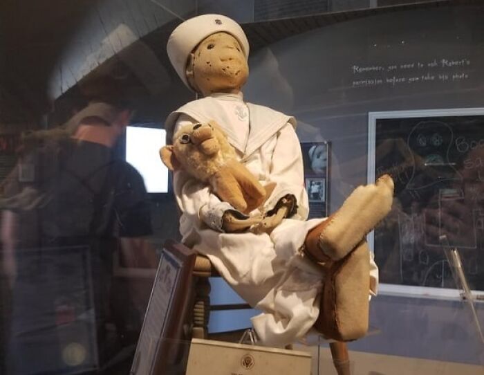 Creepy sailor doll holding a worn stuffed animal displayed in a museum, evoking unsettling Wikipedia article stories.