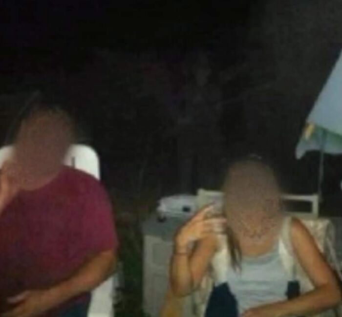 Two people sitting outside at night with a faint ghostly figure in the background, illustrating chilling ghost encounters.