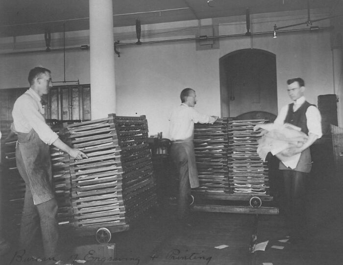 Three American working class men handling stacks of trays in a vintage industrial setting during their jobs.