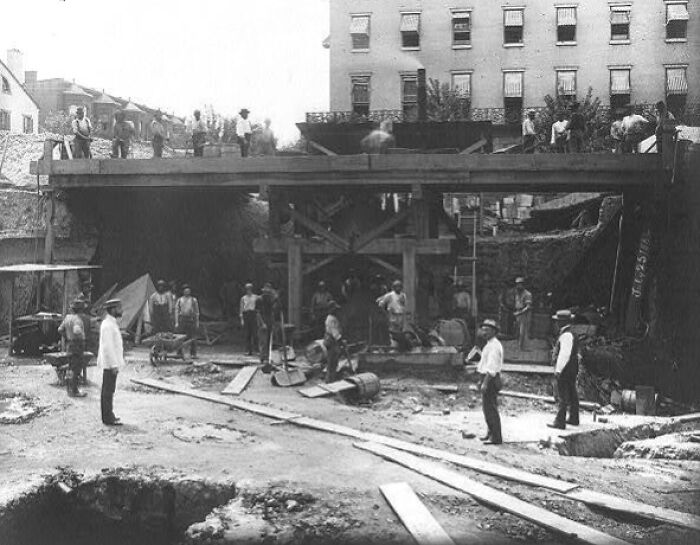 Vintage photo of American working class people laboring at a construction site beneath a bridge in an urban setting.