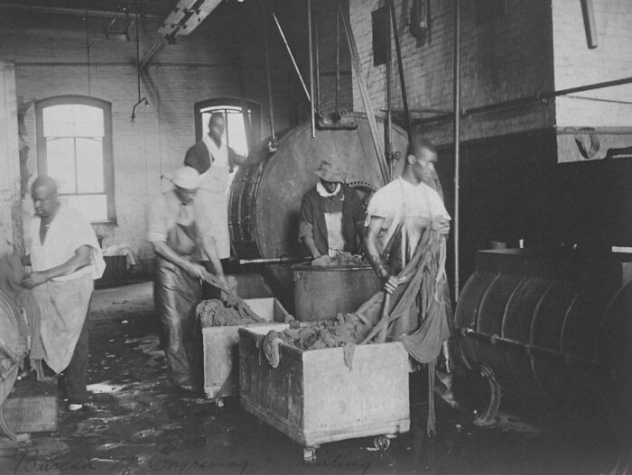 Group of American working class people in a vintage factory setting handling materials during their jobs.