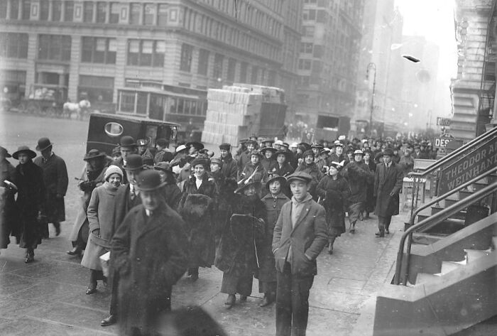 Crowded vintage street scene showing American working class people in early 20th-century clothing going about their jobs.