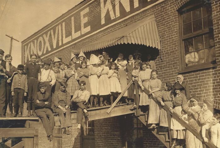 Group of American working class people posing outside Knoxville factory in a vintage black and white photo from early 20th century.