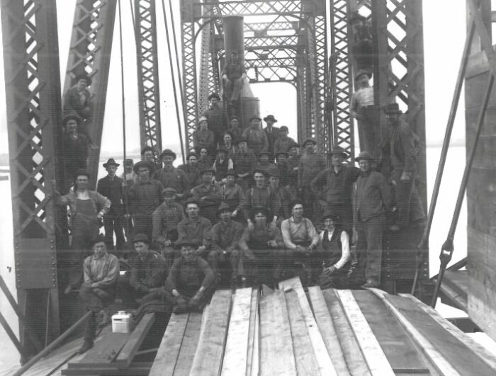 Group of vintage American working class people posing on a steel bridge construction site in the middle of their jobs.