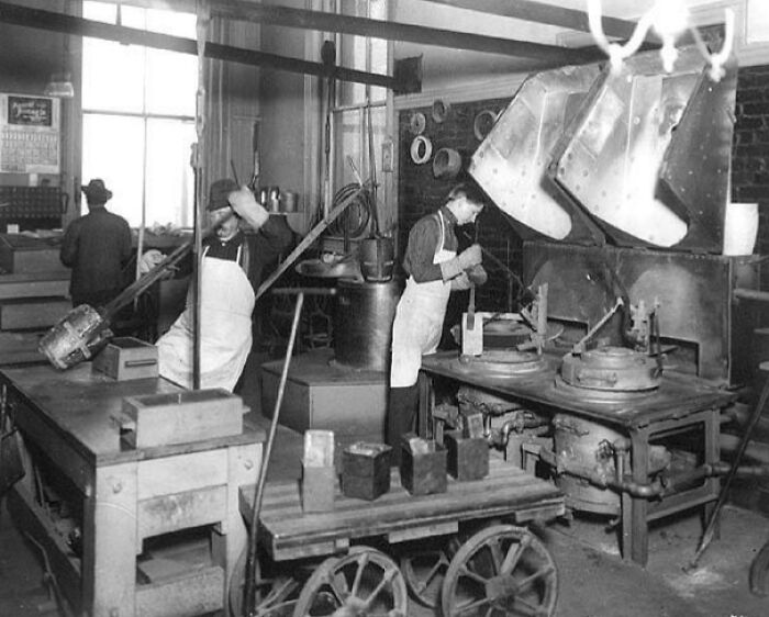 Vintage photo of American working class people in factory setting, wearing aprons and handling machinery and tools.