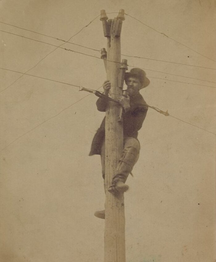 Vintage photo of an American working class man climbing a utility pole performing his job on the job site.