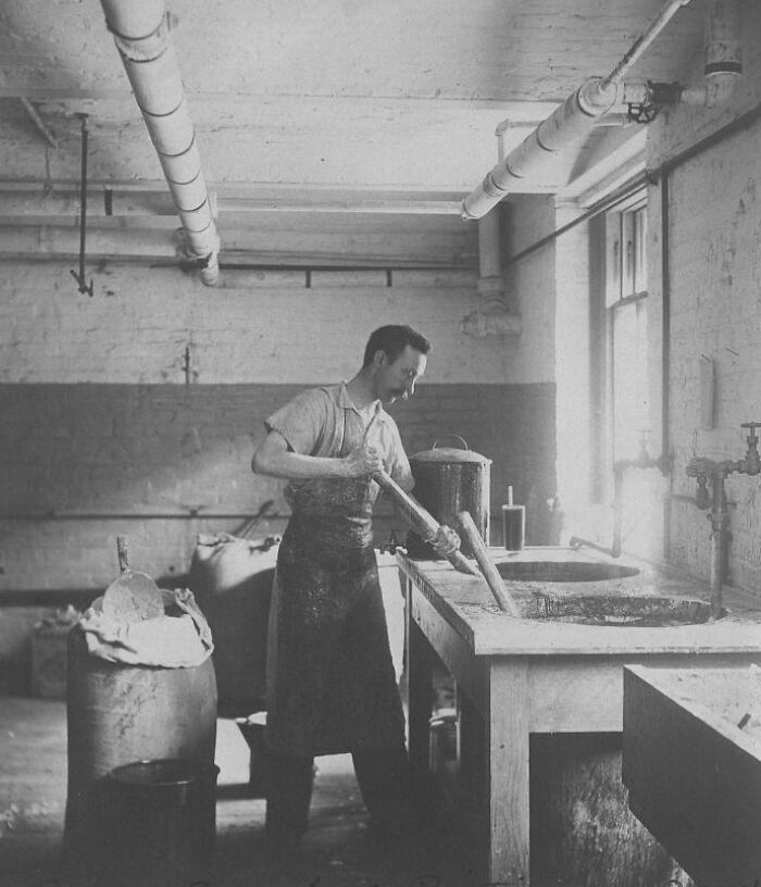American working class man in vintage photo stirring mixture in industrial workspace with pipes and window light.