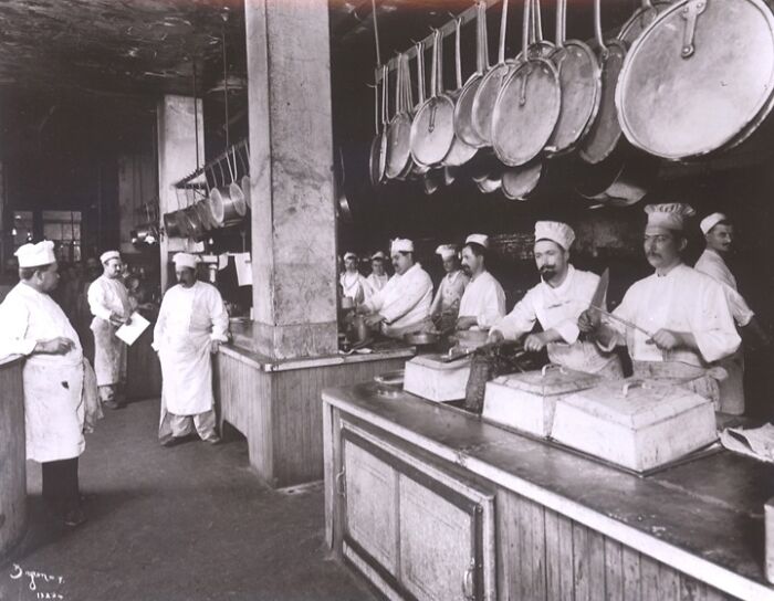 Group of vintage American working class chefs preparing food in a busy kitchen at the middle of their jobs.