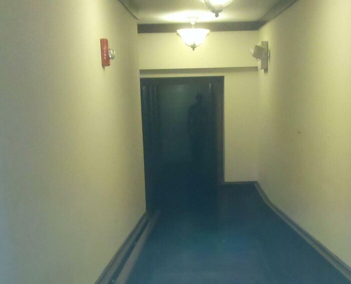 Dimly lit hallway with a shadowy figure near the door, evoking chilling ghost encounters in a haunting atmosphere.