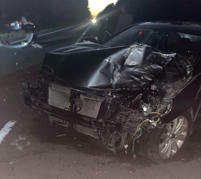 Damaged black car on a dark road at night, evoking eerie feelings linked to chilling ghost encounters stories.
