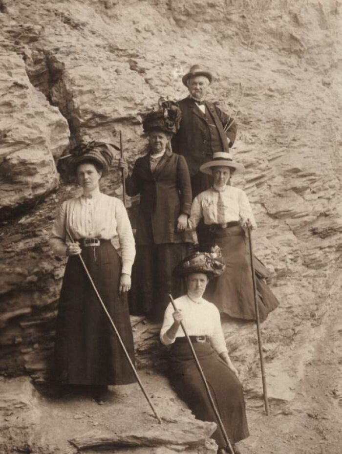 Group of Victorian-era people wearing period clothing and hats, holding walking sticks on rocky terrain, Victorian times scene.