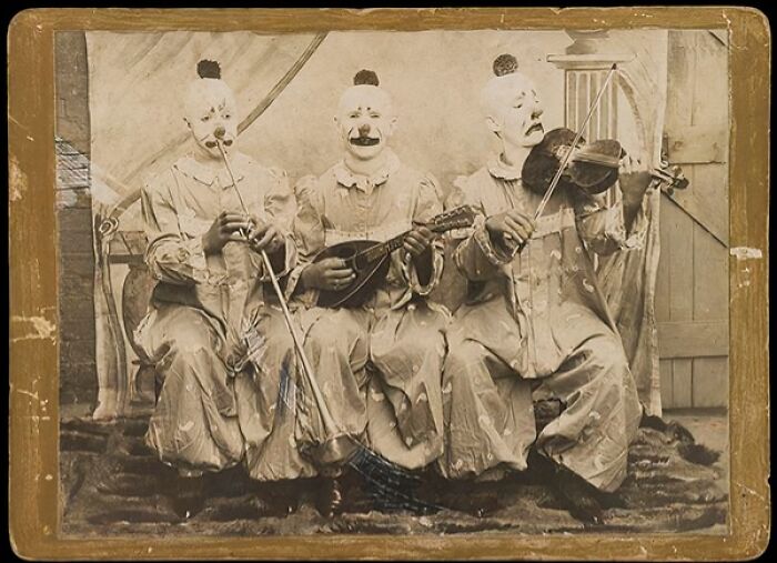 Three Victorian clowns in white face paint playing musical instruments in a strange vintage scene from Victorian times.